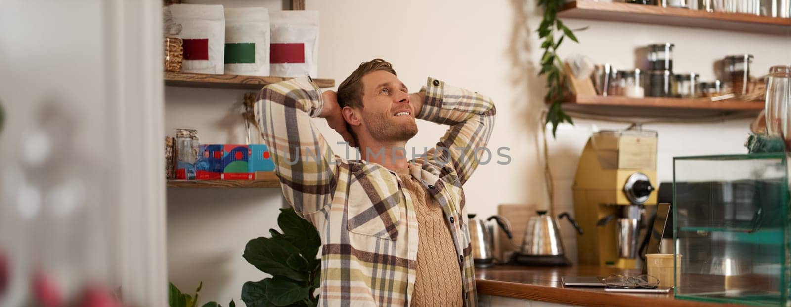 Portrait of man with pleased face, stretching after finishing work or project, freelancing, has remote job, sitting in cafe with closed laptop, smiling pleased.