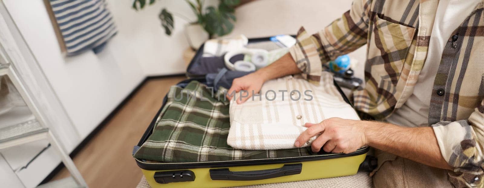 Male hands, tourist packs his clothes inside suitcase, puts items inside luggage to go on holiday, plans vacation, travels abroad.
