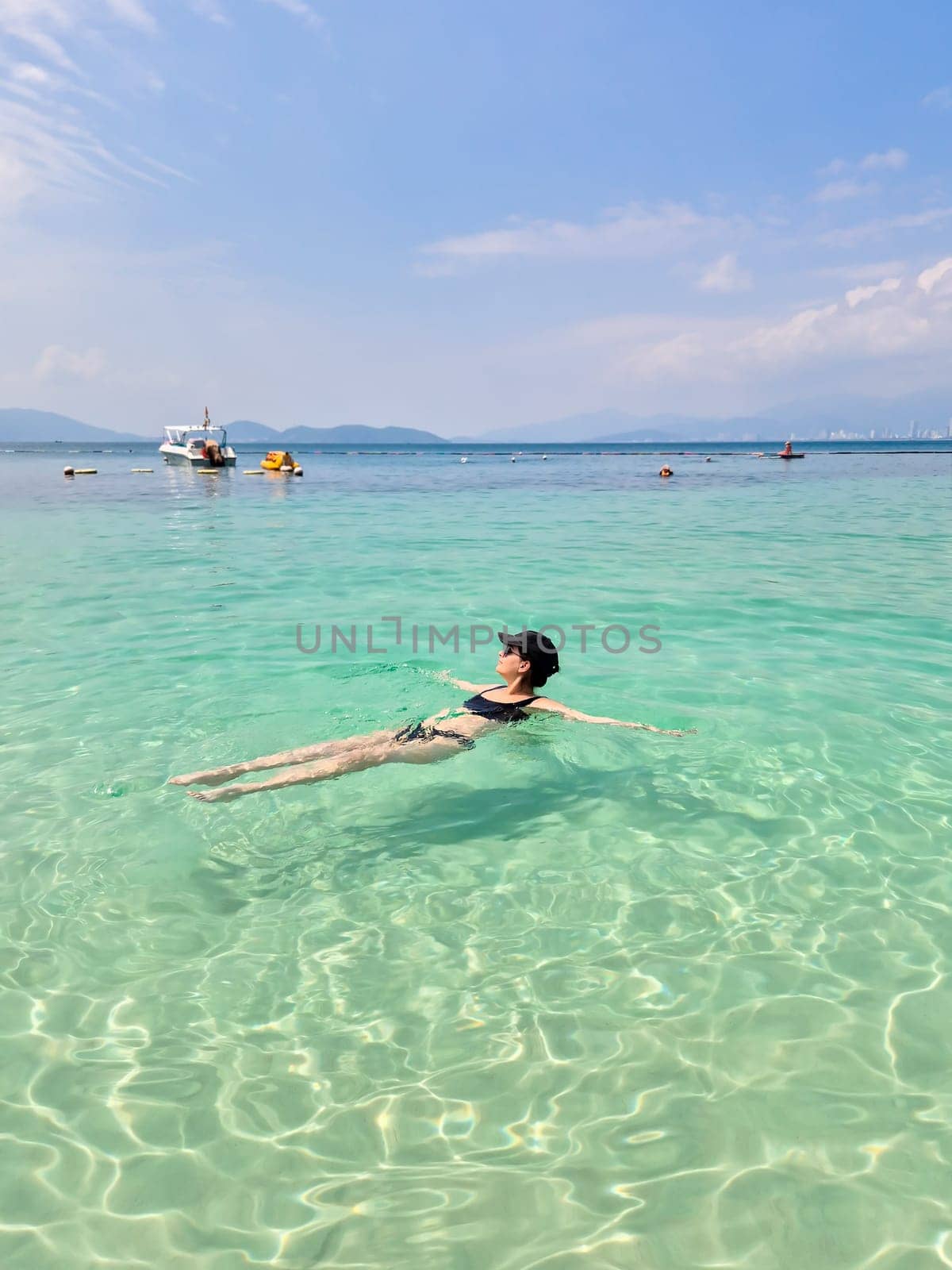 A brunette Russian girl in a black swimsuit and cap relaxes on Nha Trang beach. Sunny day, South China Sea, Vietnam.