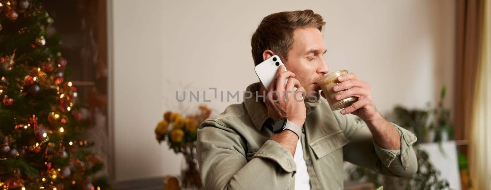 Close up portrait of handsome man enjoys his coffee, drinks cappuccino, talks on mobile phone, answers a phone call, sits in cafe.