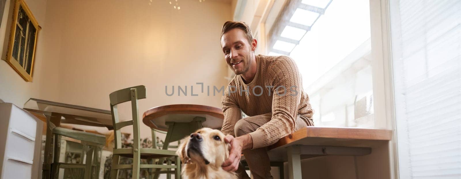 Vertical shot of young smiling man with his dog, golden retriever pet in a cafe.