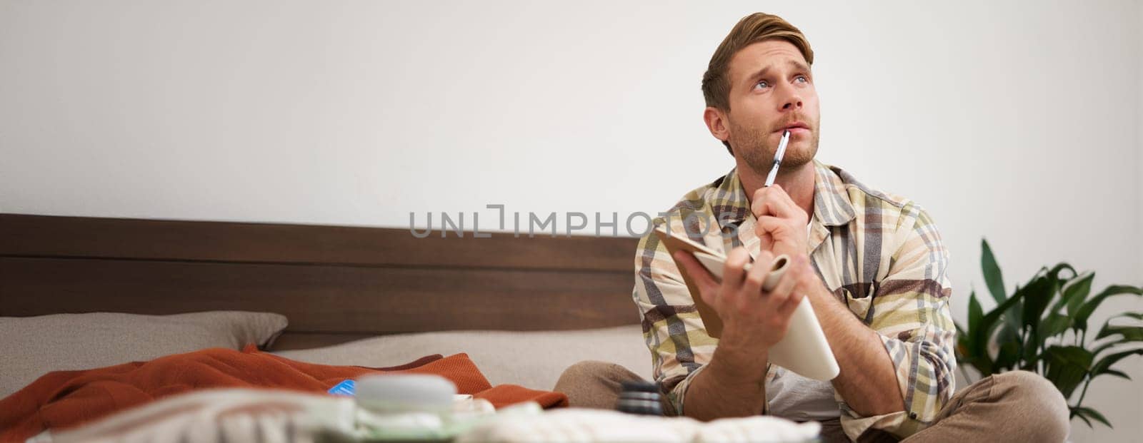 Portrait of thoughtful young man, tourist going on vacation, going through holiday check-list, writing down what he wants to take on travelling.