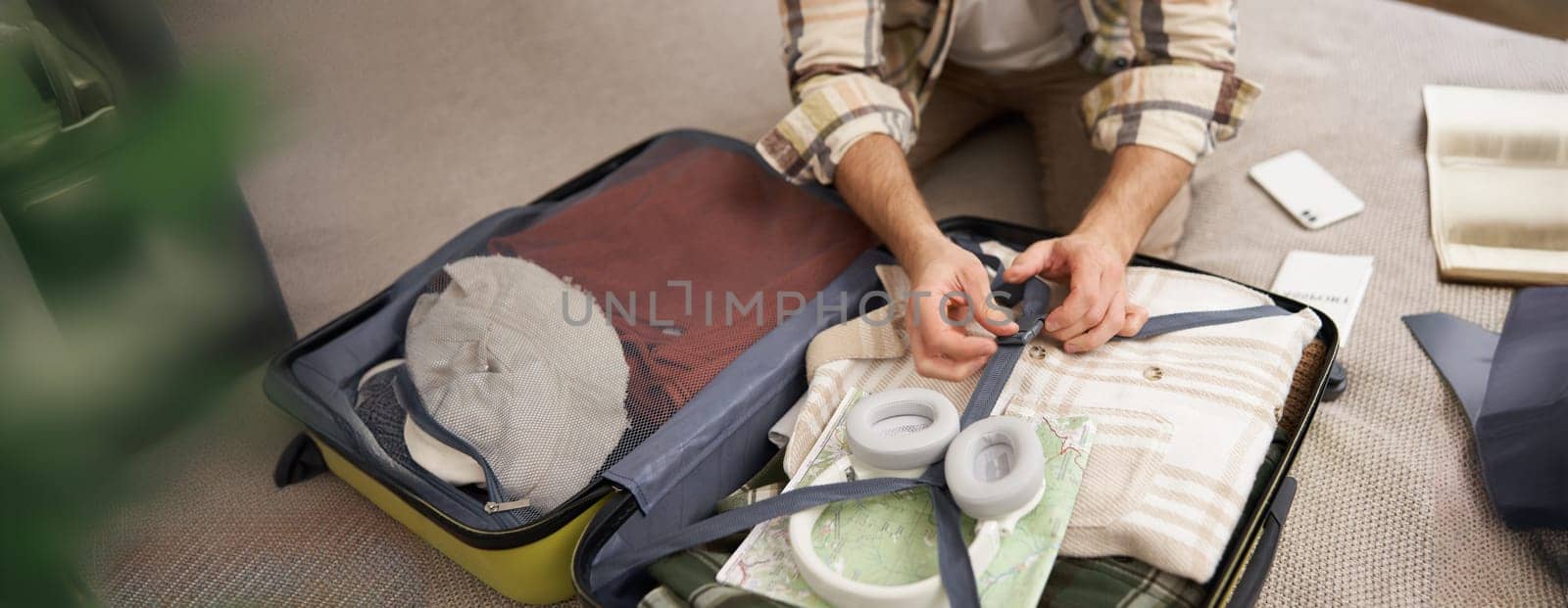 Close up portrait of male hands, man putting clothes inside suitcase, packing for holiday. Tourism and travelling concept