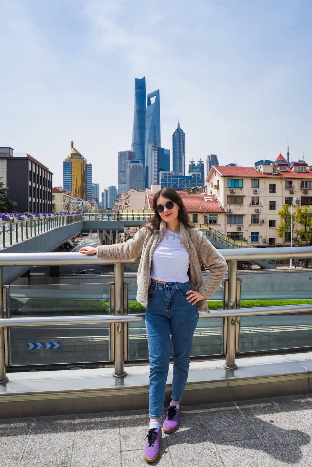 Brunette in sunglasses smiles at camera on Shanghai viaduct with Pudong skyline featuring Shanghai Tower, World Financial Center and Jin Mao Tower behind her