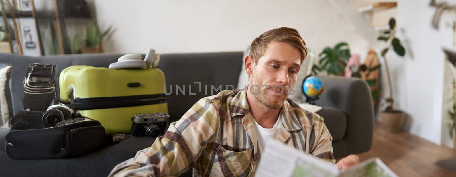 Portrait of man, traveller looks confused at map, studying the route to go on vacation or business trip. Tourism concept
