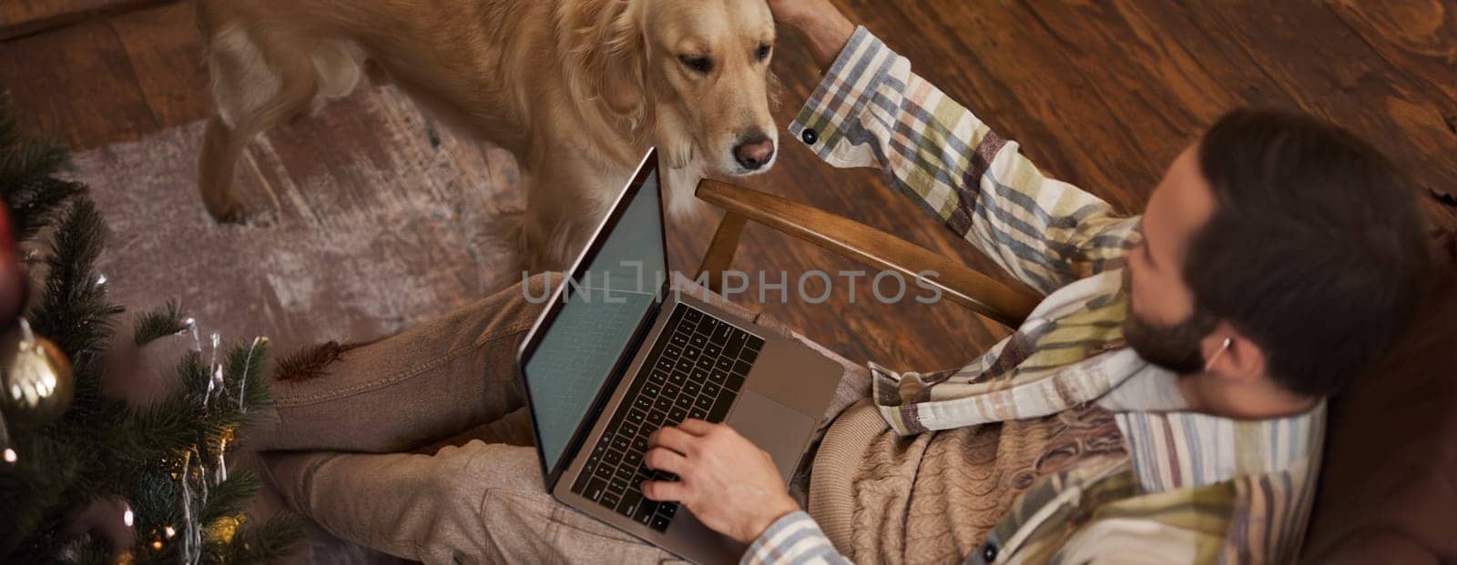 Vertical cropped photo of male hands and body, man petting the dog while working on laptop in cafe, drinking coffee.