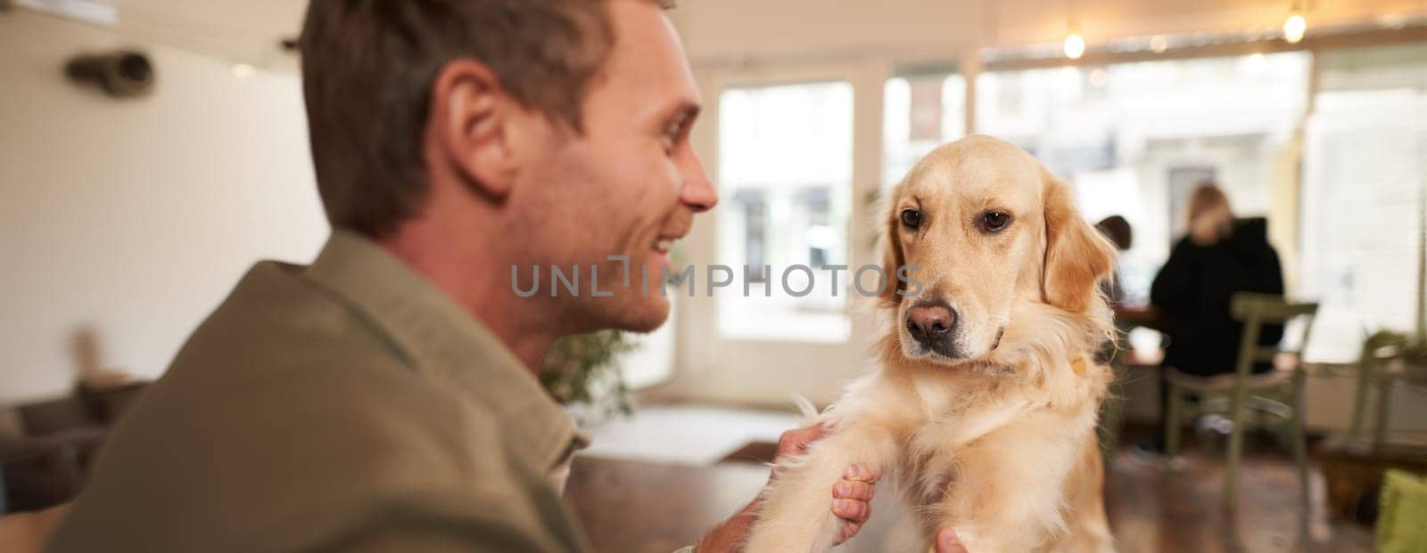 Close up portrait of young man with his pet in coffee shop. Dog owner playing with his pet, looking happy.
