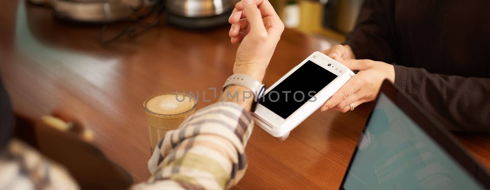 Man in cafe paying contactless using his digital watch on wrist, holding it close to the POS contactless terminal, working from coworking.