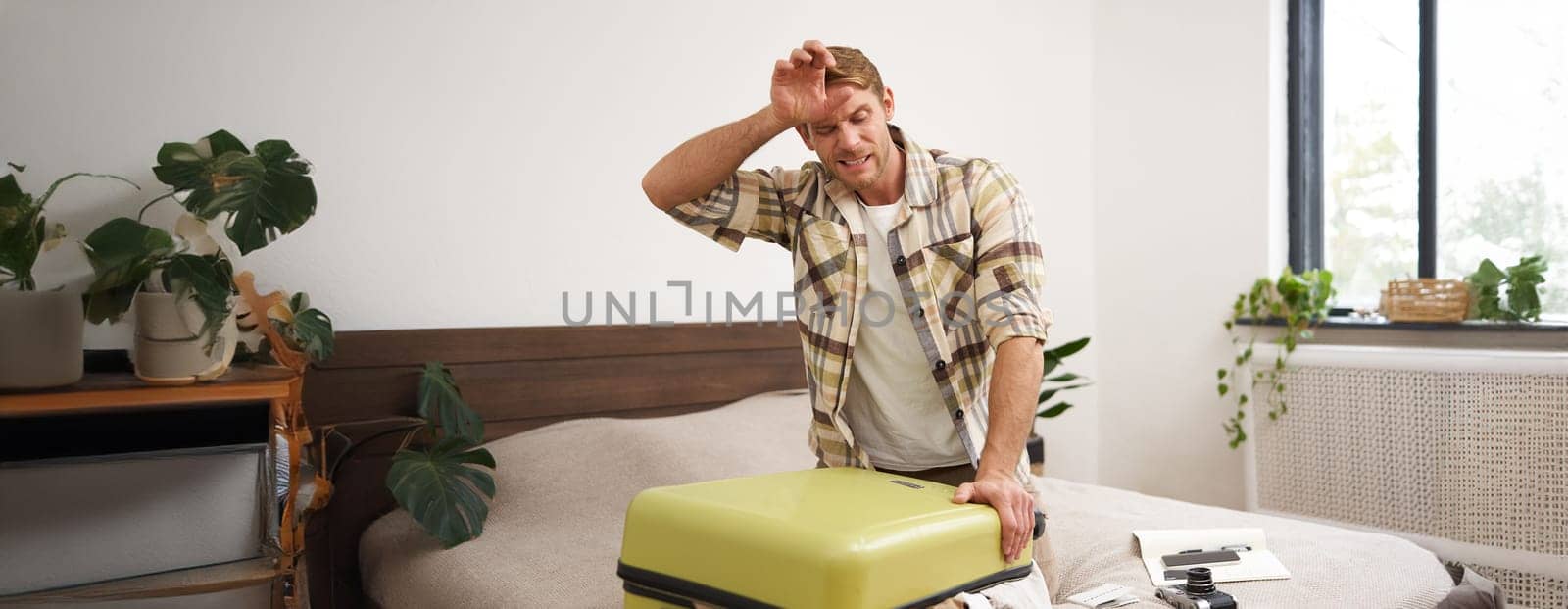 Portrait of man struggling to close suitcase full of clothes, putting effort to pack luggage for holiday, going on long vacation. Tourism and travel agency concept