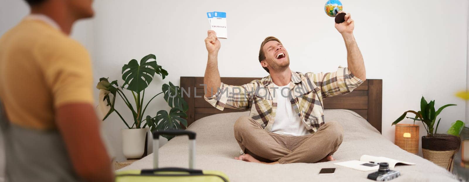 Image of happy smiling man, cheerful tourist sits with globe and plane tickets, goes on holiday, sits with suitcase, excited about his trip, going on holiday. Tourism and travel agency concept