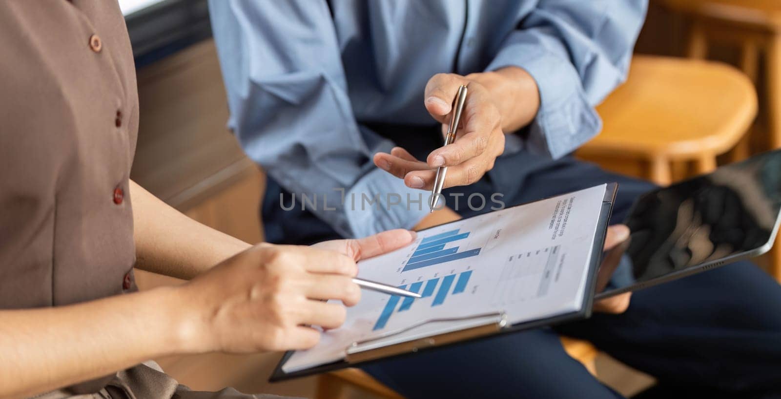 Two business professionals engage in a collaborative discussion, analyzing financial data and charts on a tablet in a contemporary office setting.