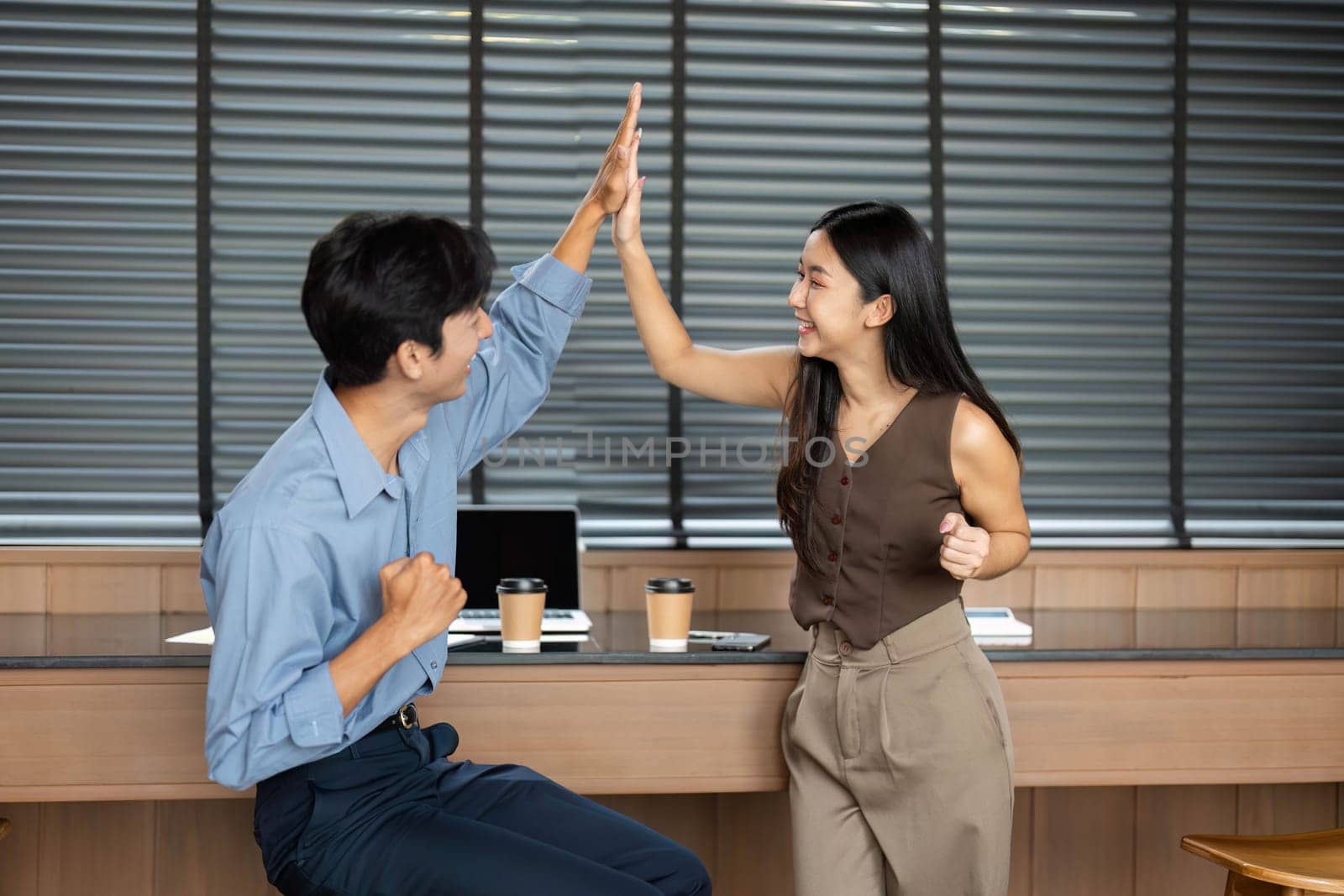 Two young professionals sharing a high-five, celebrating a successful collaboration in a bright office space.