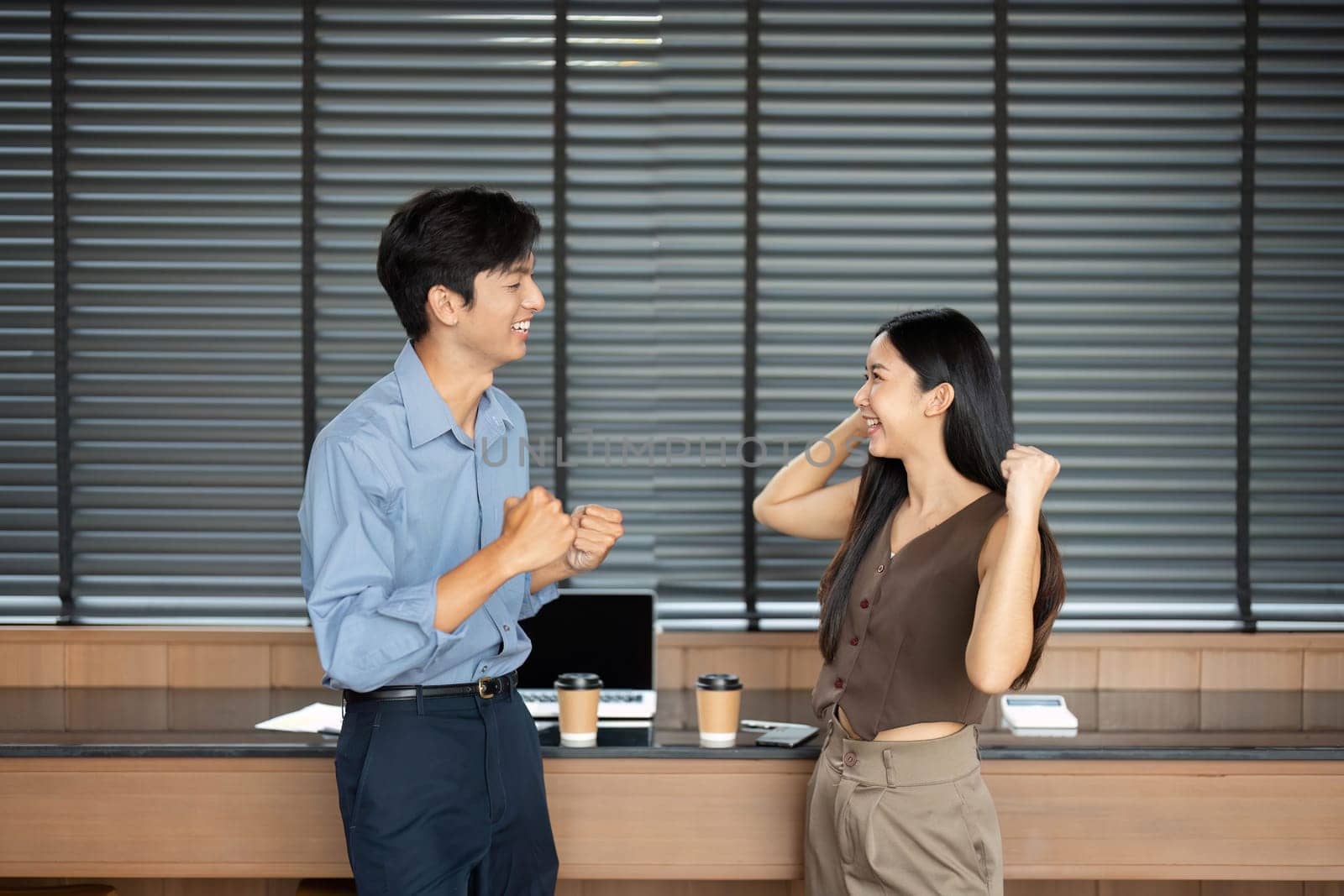 Two young professionals joyfully celebrating their achievements together in a modern office setting.