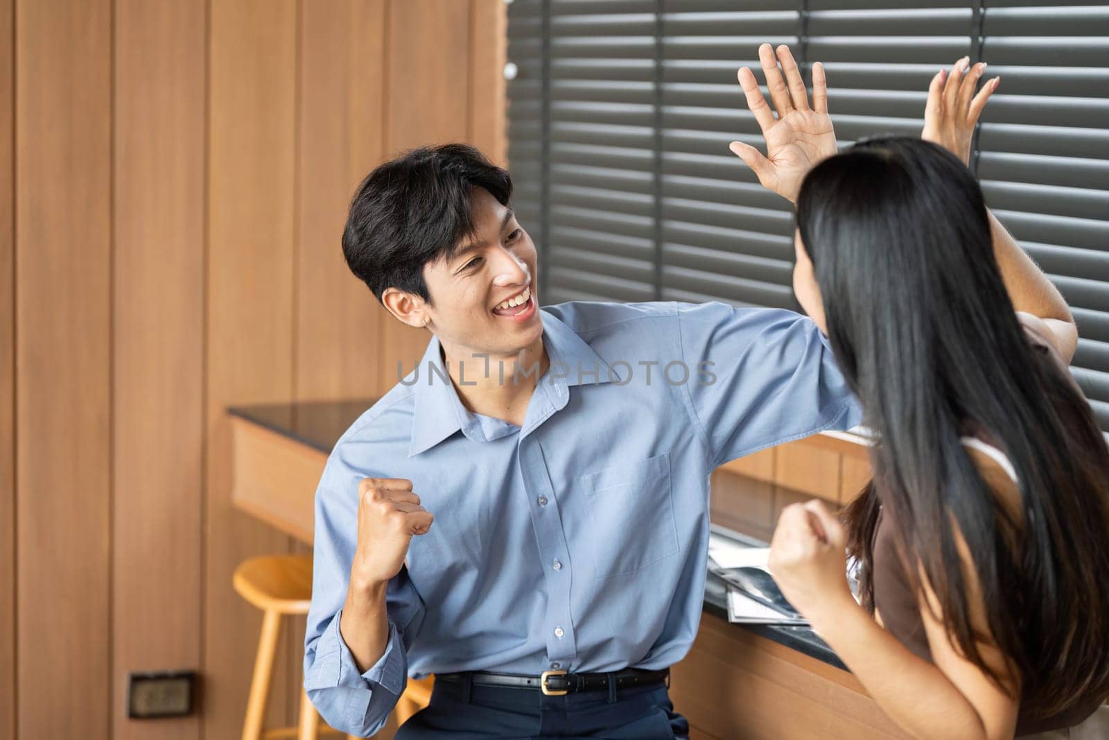 A young man and woman celebrating their success with high-fives in a modern workspace, representing teamwork and motivation.