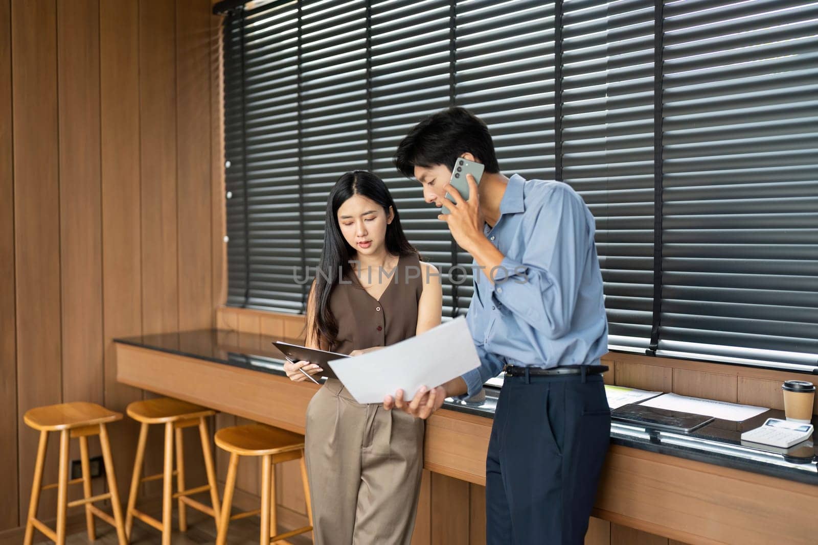 A businesswoman and businessman analyze project documents together, showcasing teamwork and collaboration in a modern workspace.