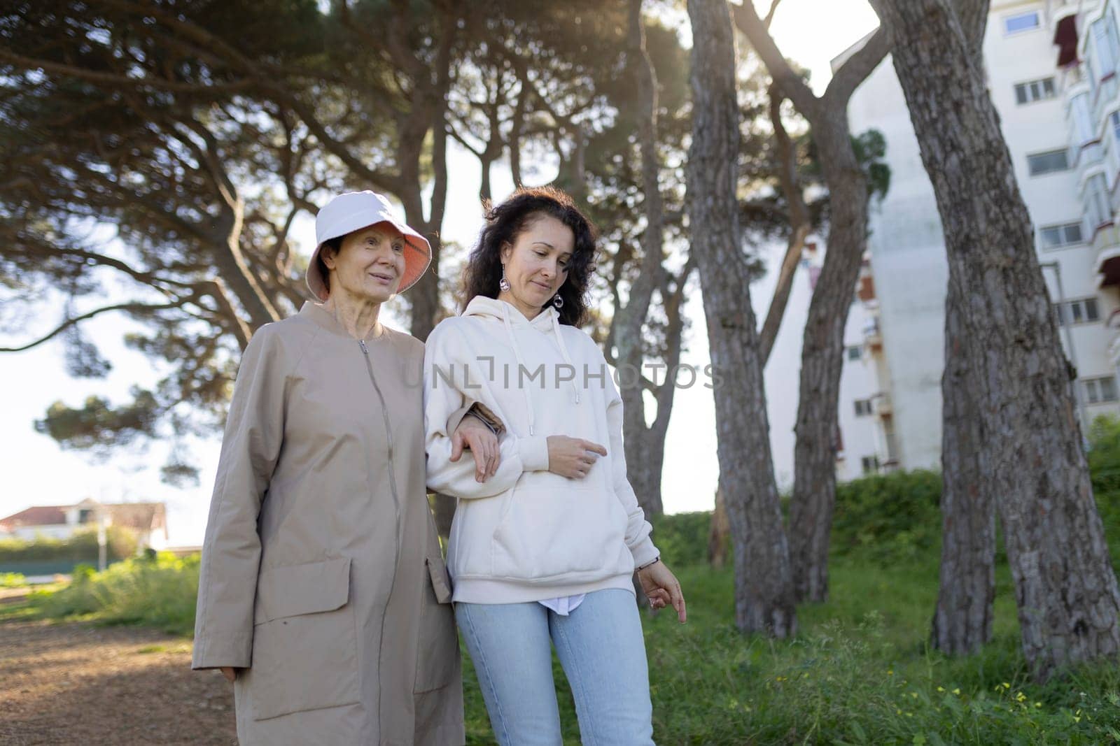 Senior woman and her daughter walking arm in arm in a park, enjoying a sunny day together