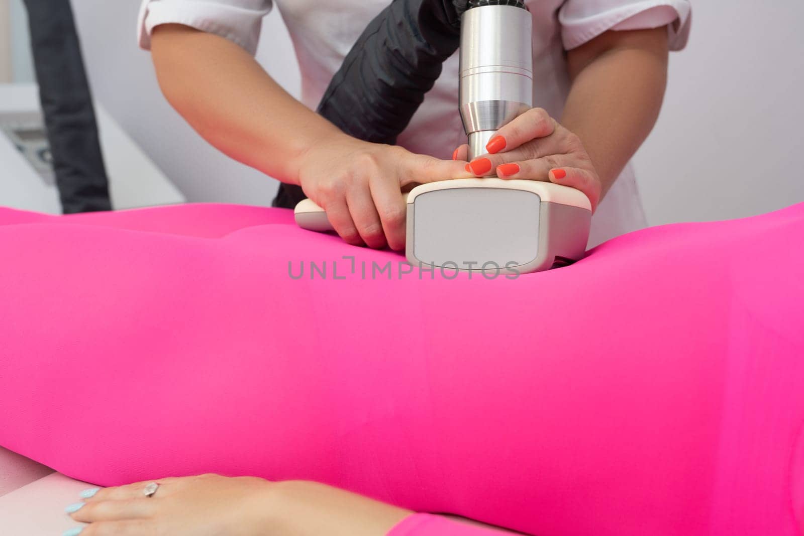 Crop anonymous masseur massaging body of unrecognizable female client in anti cellulite suit with modern apparatus in clinic