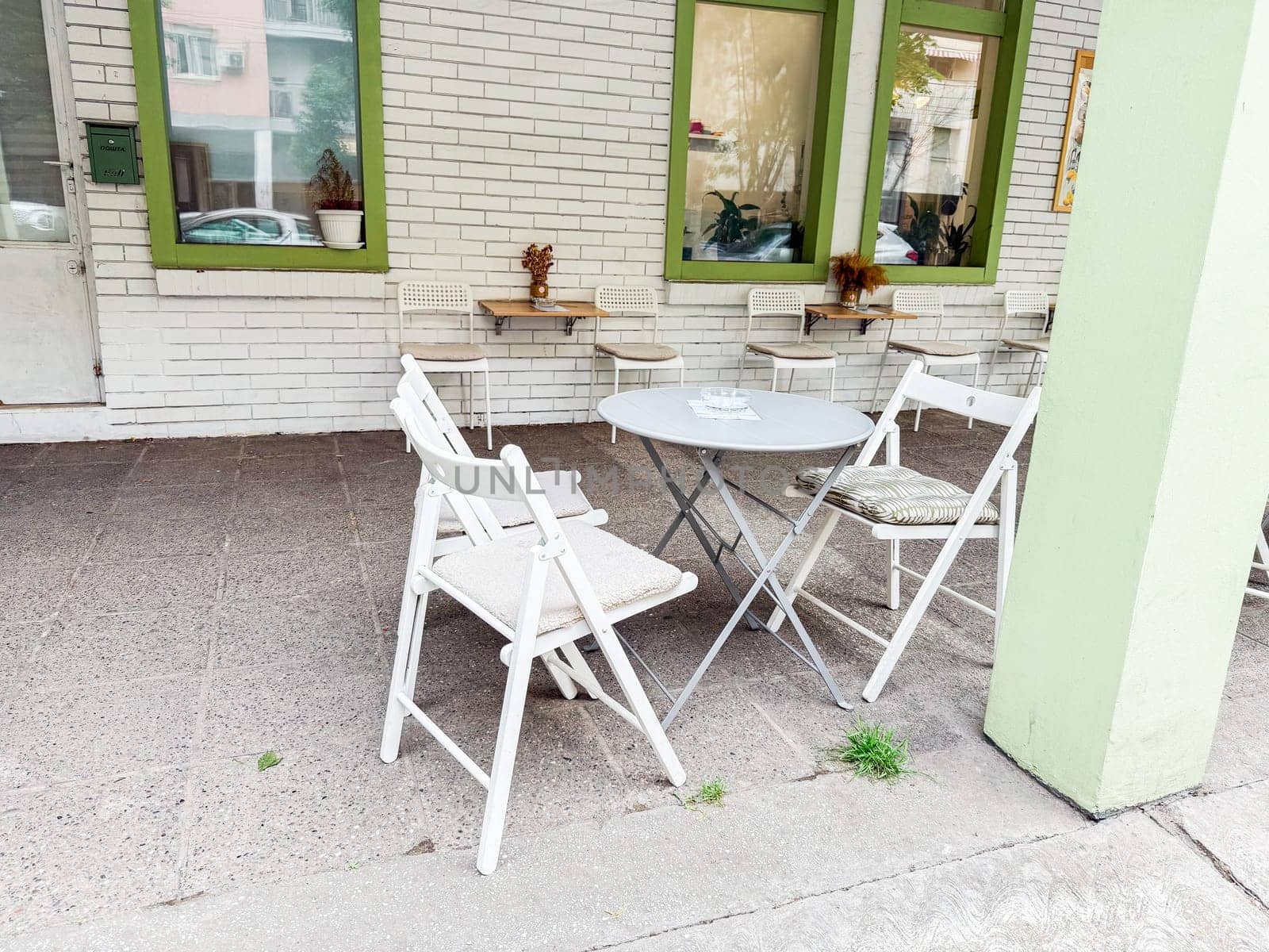 Simple cafe patio with folding white chairs and round metal table against brick wall. Casual street dining and social outdoor space.