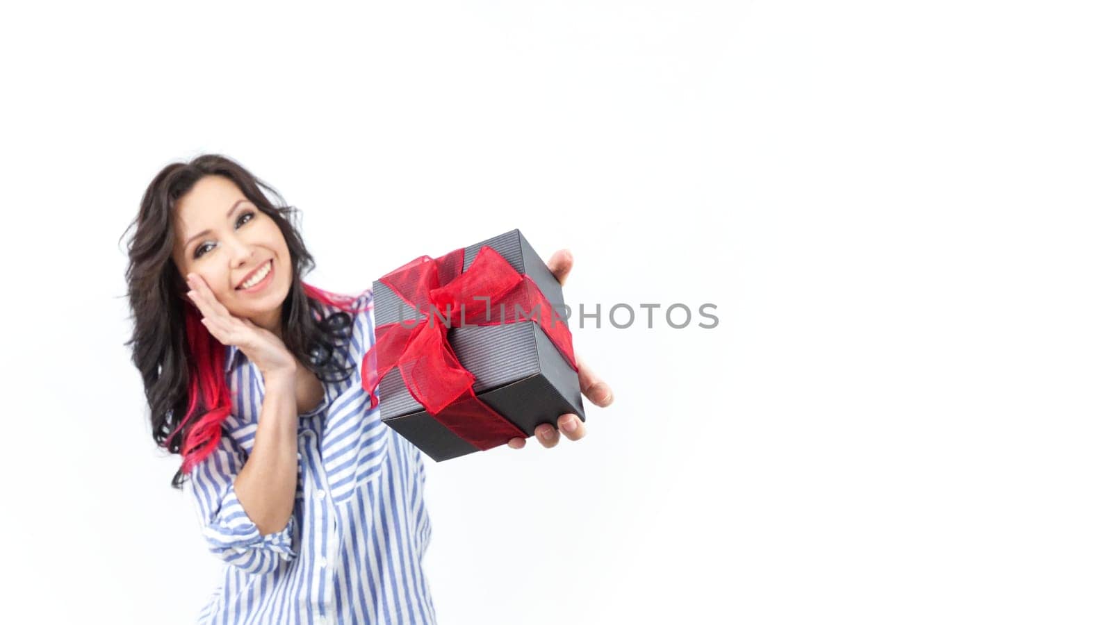 A cheerful woman looks at the camera with a warm smile, wearing a trendy casual outfit. Her long, dark hair enhances the soft, neutral background, creating a joyful and inviting atmosphere.