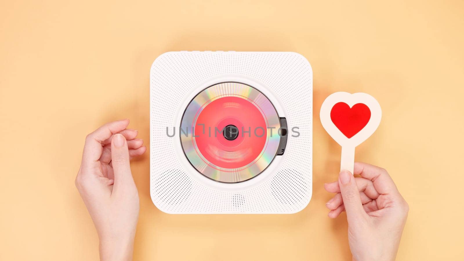 A vintage white retro styled portable compact disc player sits next to a vibrant red heart-shaped object, beautifully isolated on a soft peach background, creating a nostalgic and romantic atmosphere.