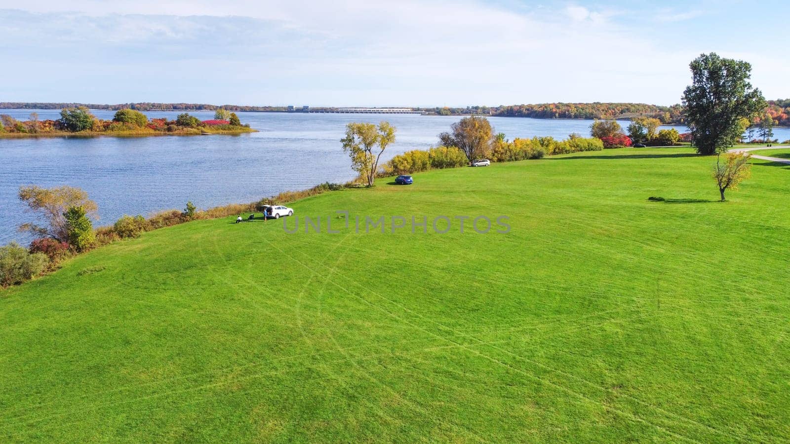 Ottawa, ON Canada - 2024-06-20: Expansive Green Field Surrounded by Peaceful Lake and Beautiful Blue Sky with Clouds.