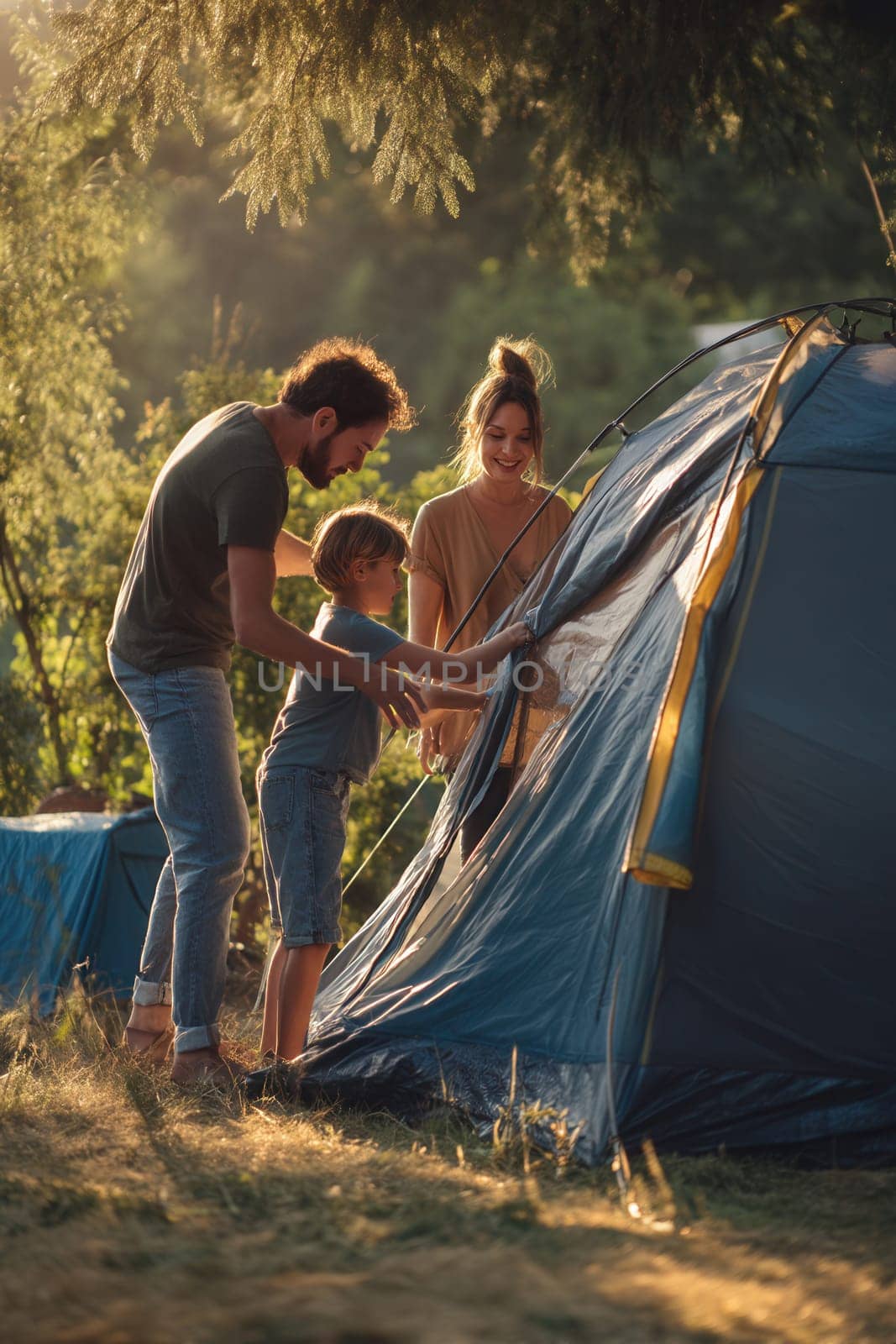 A happy family with their young son sets up a tent in the forest at golden hour. Great for portraying outdoor lifestyle, family bonding, parenting, and summer adventures in nature