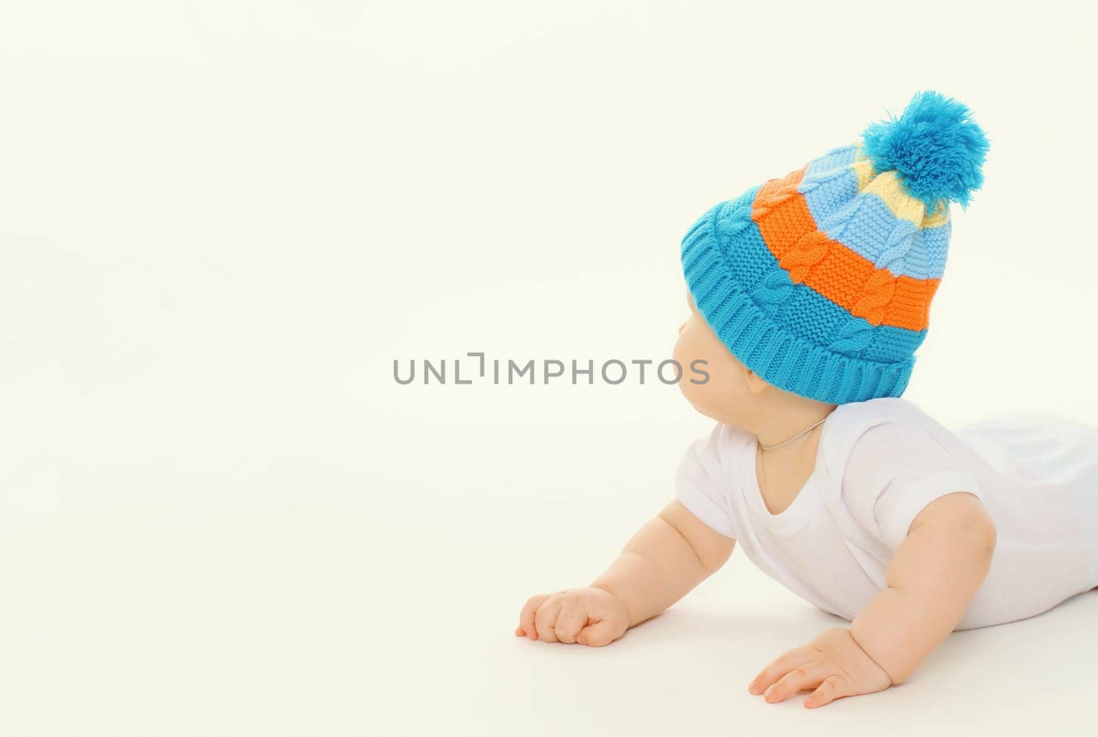 Happy cute baby in winter knitted hat crawling on the floor playing on white studio background