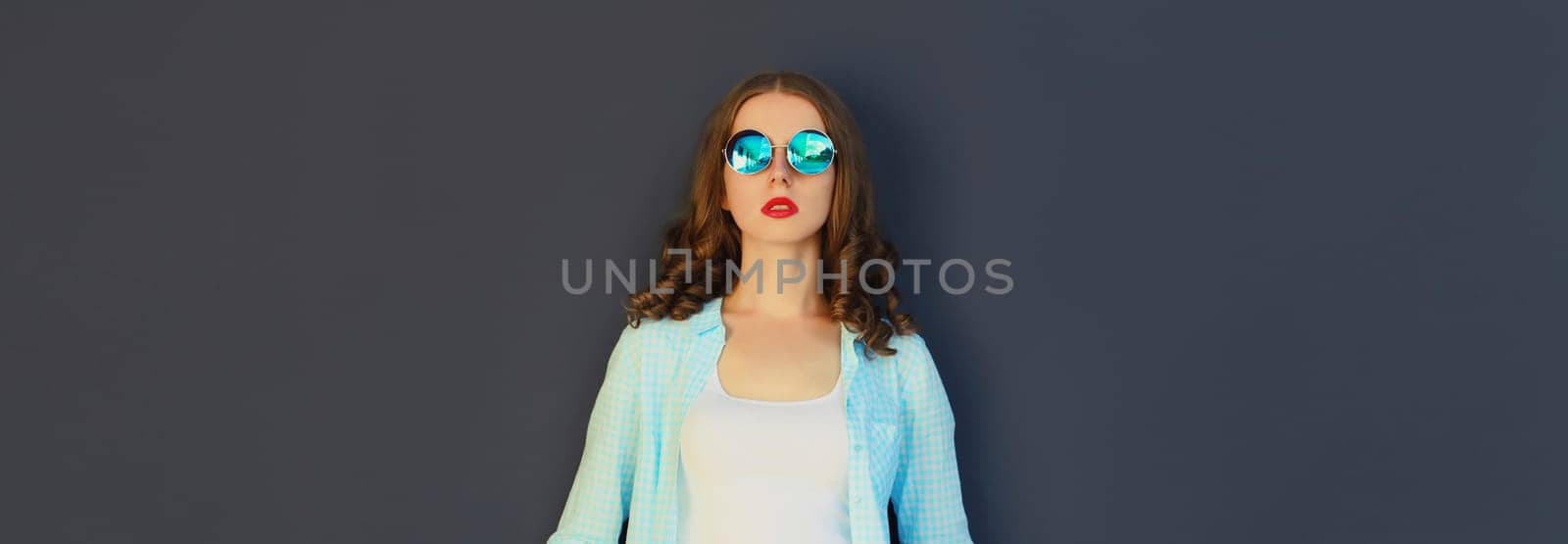 Portrait of stylish modern young woman in glasses, posing on black wall background