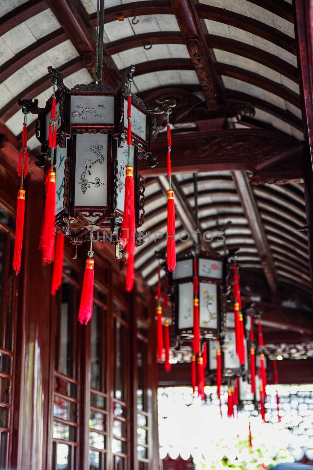 Shanghai, China - 1 April 2025: Traditional Chinese lanterns with red tassels hanging under a curved wooden roof in Yu Garden, a famous historical site in Shanghai
