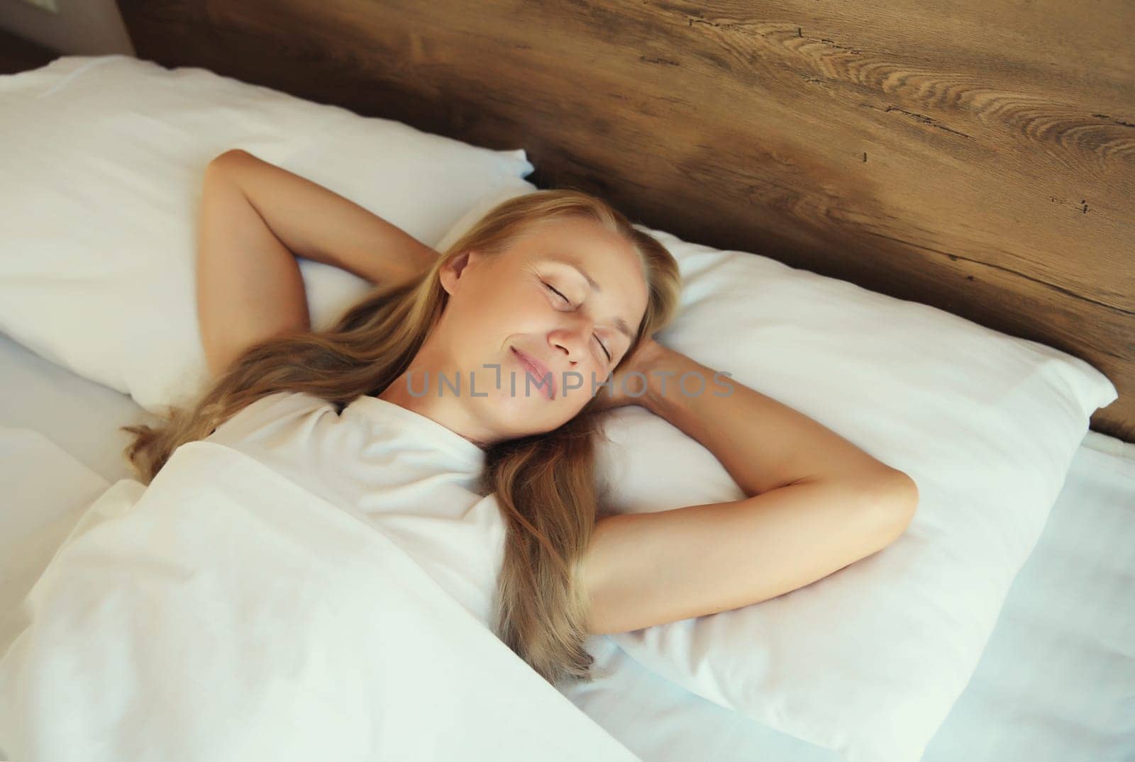 Happy young woman sleeping lying in bed on white soft comfortable pillow in bedroom at home