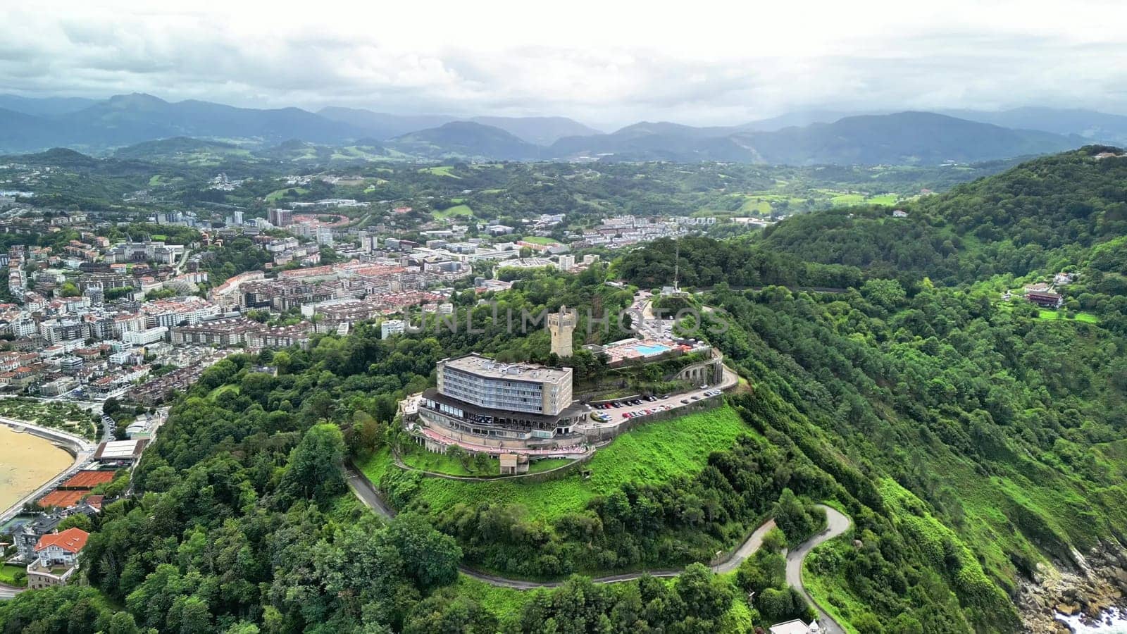 An aerial view shows a beautiful hilltop resort with stunning city panoramas and lush green hills around it