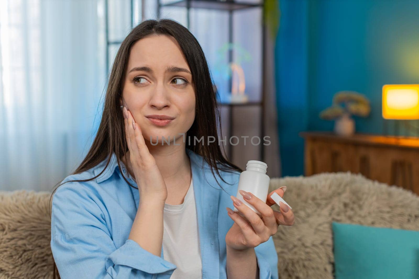 Young ill woman at home suffering from severe toothache, holding cheek painfully, tiredly searching for painkiller pills. Caucasian sick girl experiencing strong discomfort, exhausted by dental pain