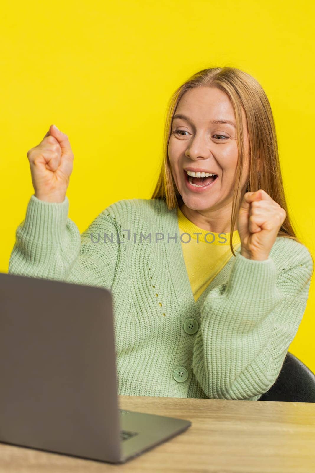 Happy Caucasian middle-aged business woman working on laptop netbook shocked by victory celebrate winning goal achievement, good email career news sitting at table isolated on yellow background indoor