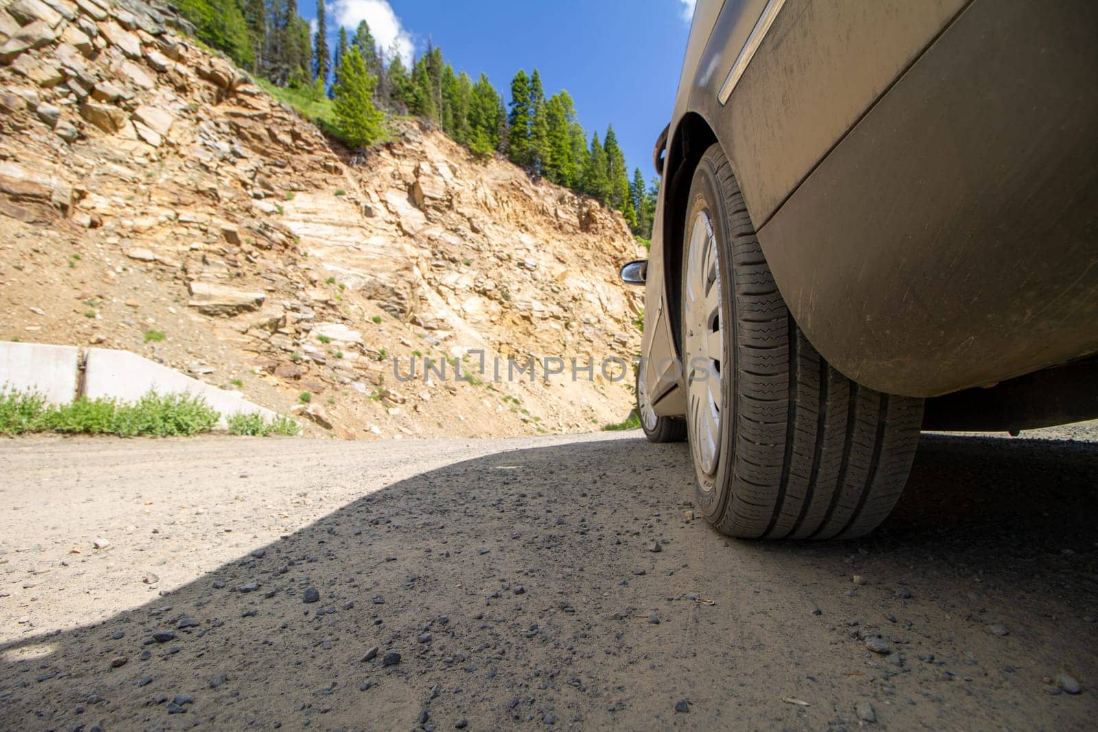 A car is parked on a dirt road next to a rocky hill. The car is dirty and the road is bumpy