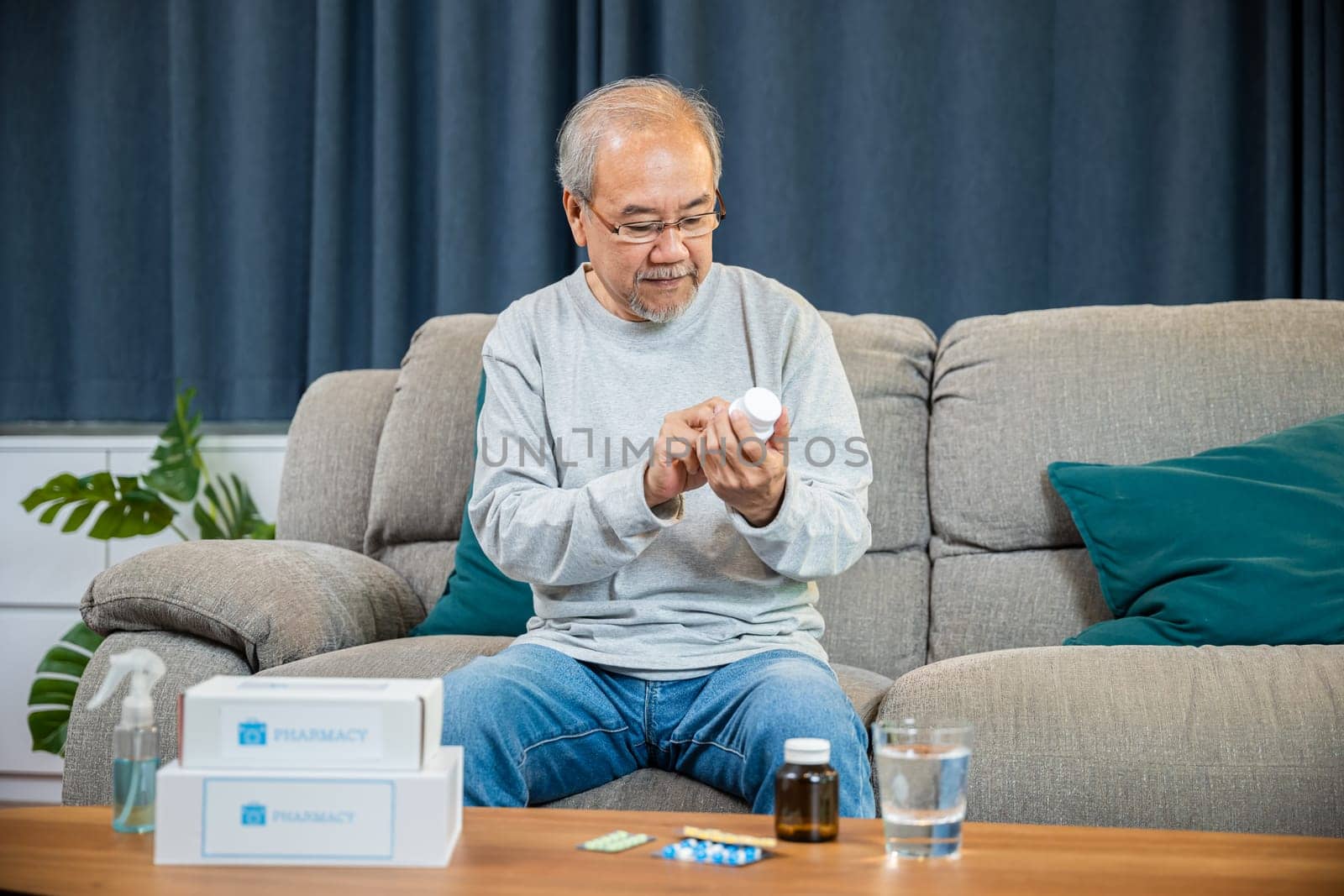 Asian worried senior man with medicine pills to taking on table in the living room, old man buy herbal self cure Rx pill online from pharmacy, home isolation, health care help service