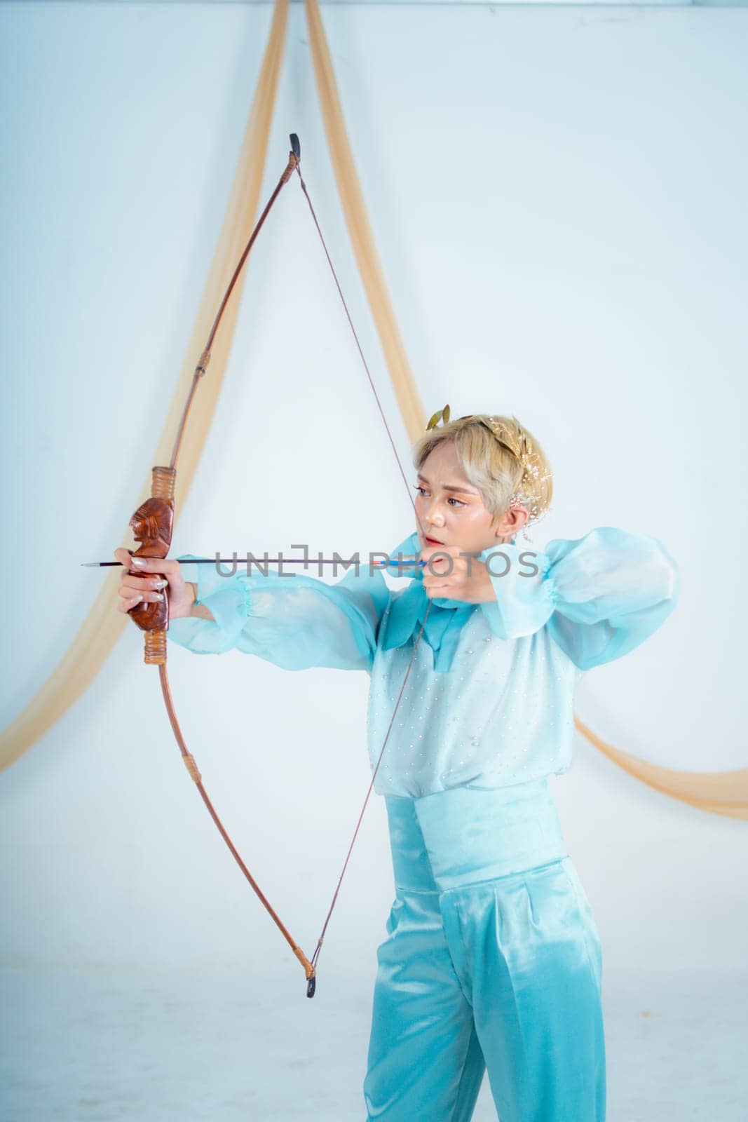 an Asian woman with blonde hair holding an arrow while wearing a blue dress in a white room
