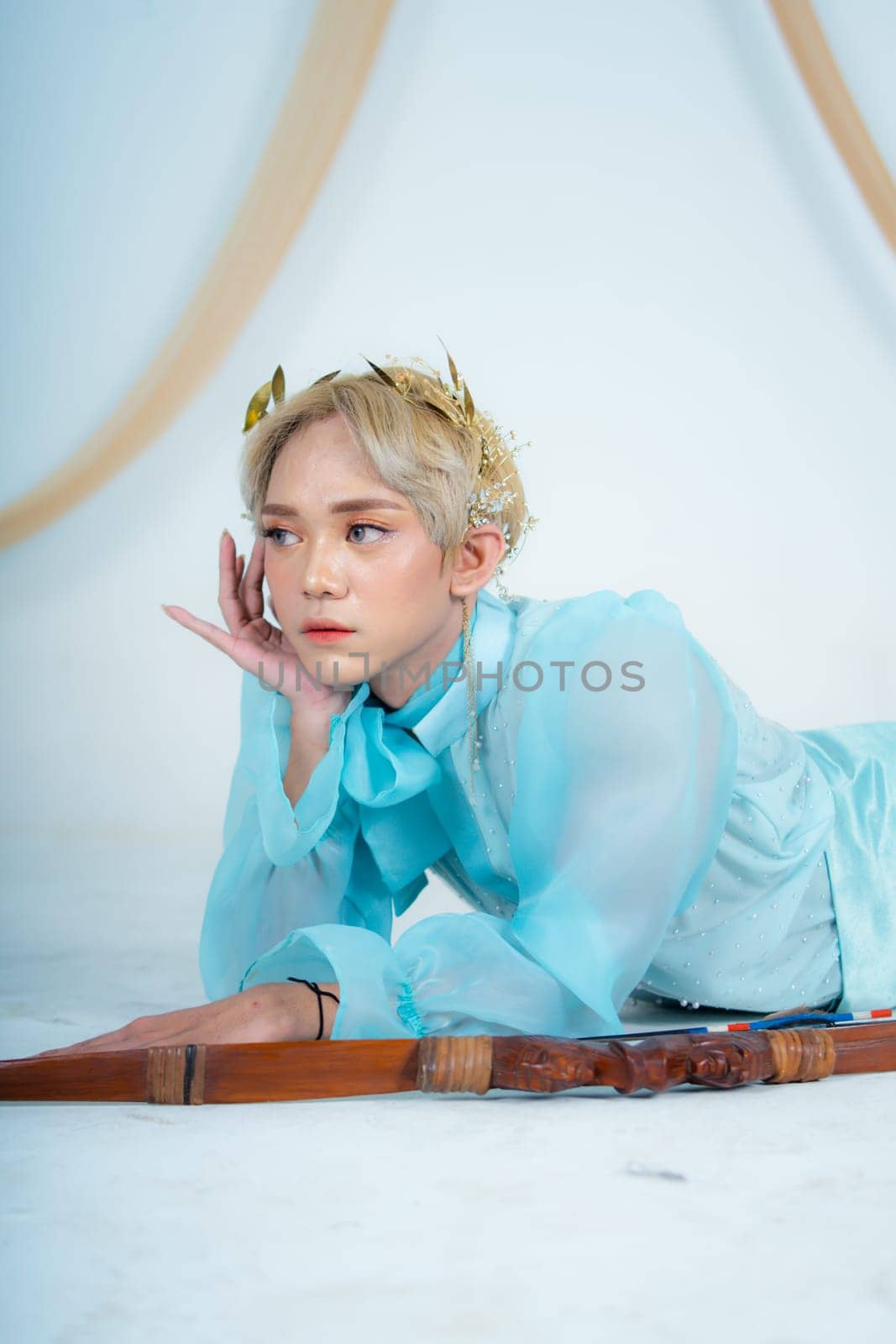 a woman with blonde hair and a face full of makeup poses beautifully with a bow in a white studio