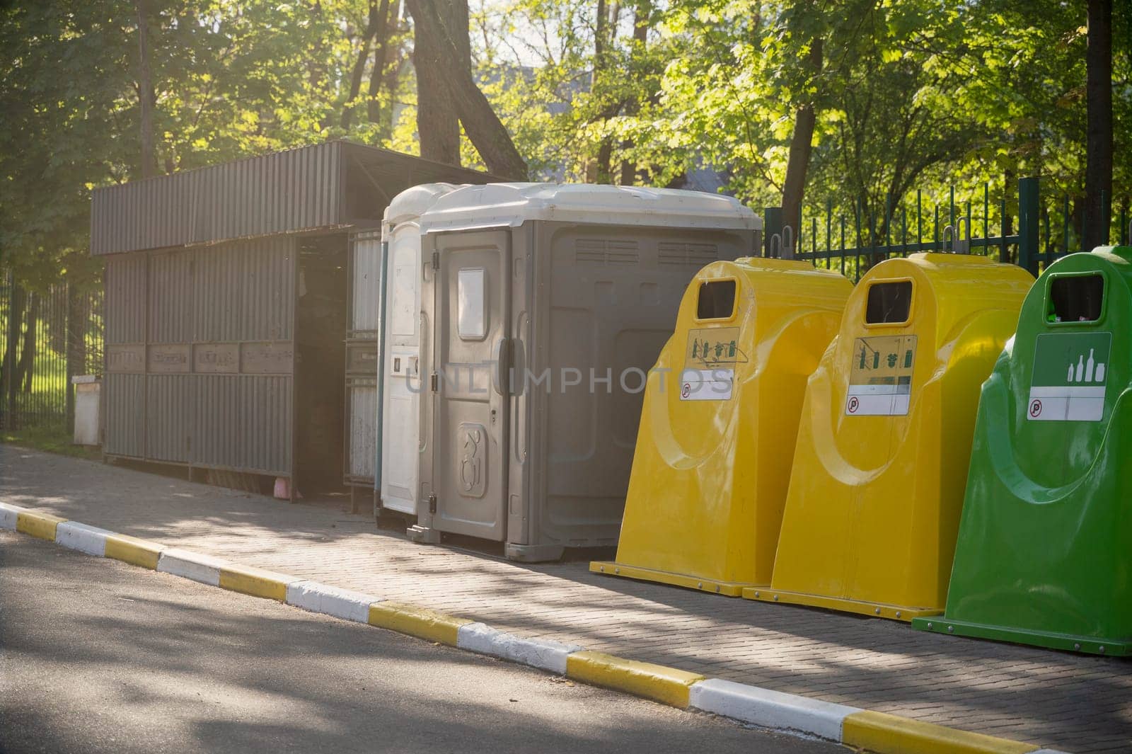 Containers for waste collection and recycling in the city park, and a bio-toilet for people with disabilities. Yellow, blue containers for recycling plastic, paper and glass waste.