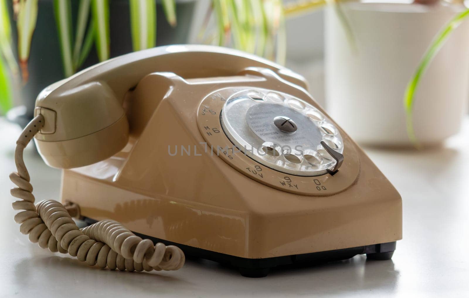 A vintage phone with a cord hanging off it. The phone is tan