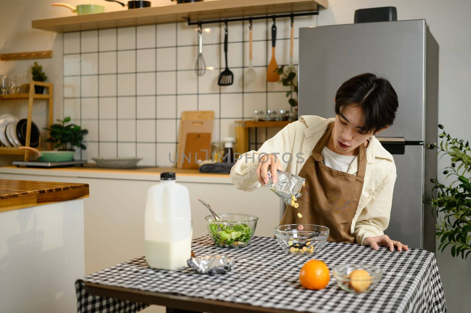 Young man pouring cereal into bowl for breakfast at home kitchen table.
