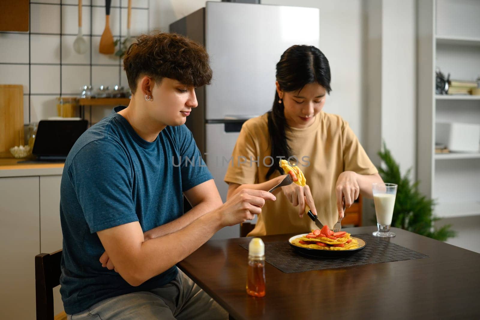Happy couple enjoying homemade pancakes together at breakfast table.