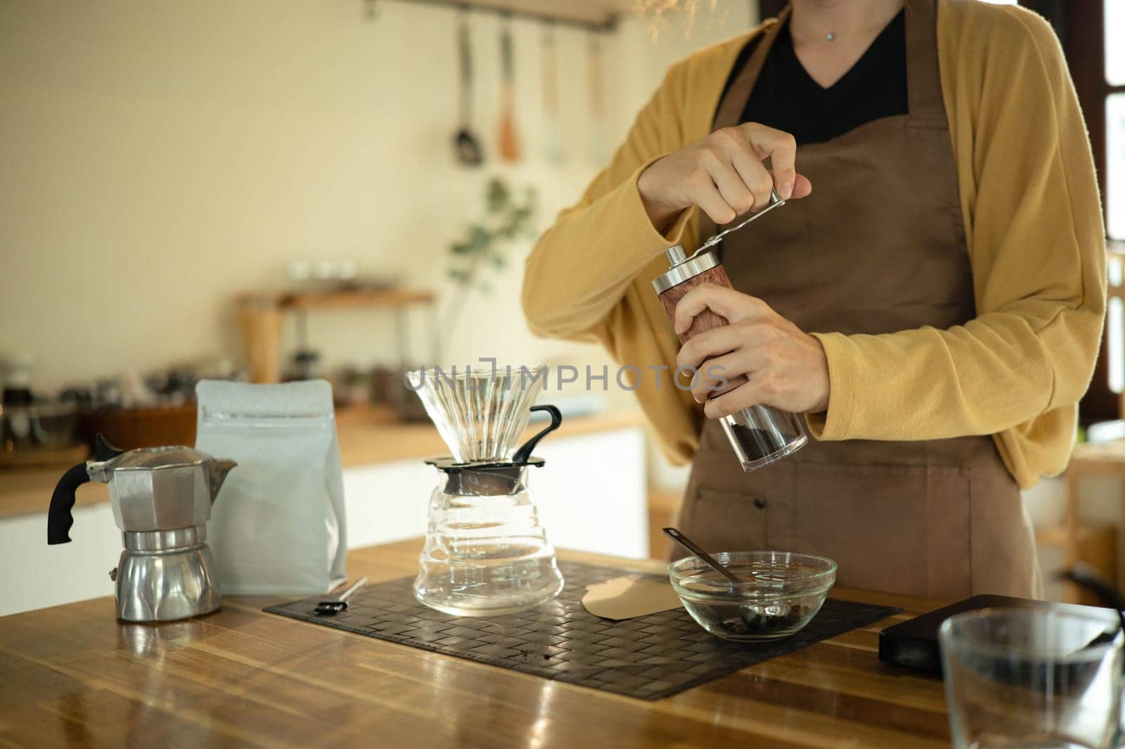 Young woman grinding coffee beans by hand in a kitchen preparing for fresh pour over brew.