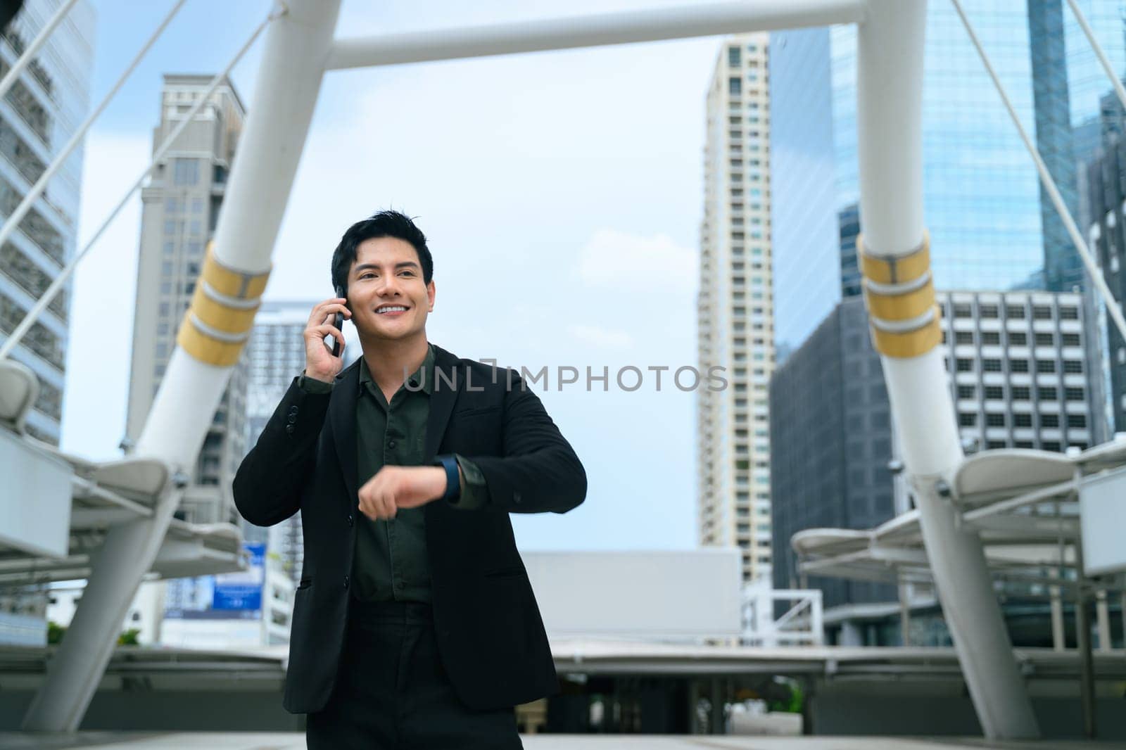 Confident businessman checking time on smartwatch, standing in a modern city.