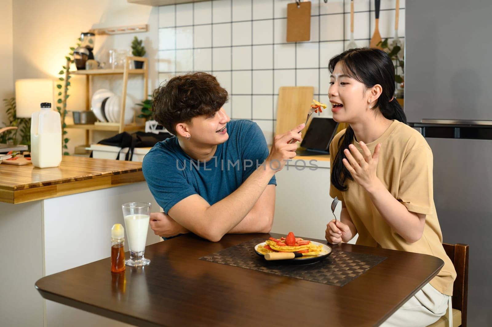 Happy couple enjoying homemade pancakes together at breakfast table.
