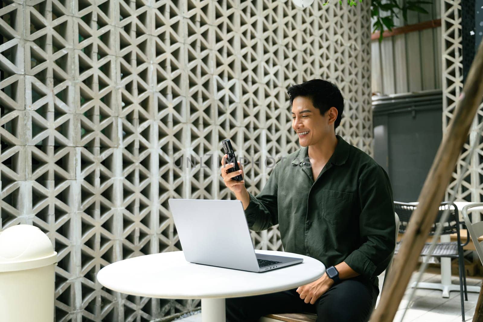 Smiling man having video call while working remotely on laptop at an outdoor urban cafe.