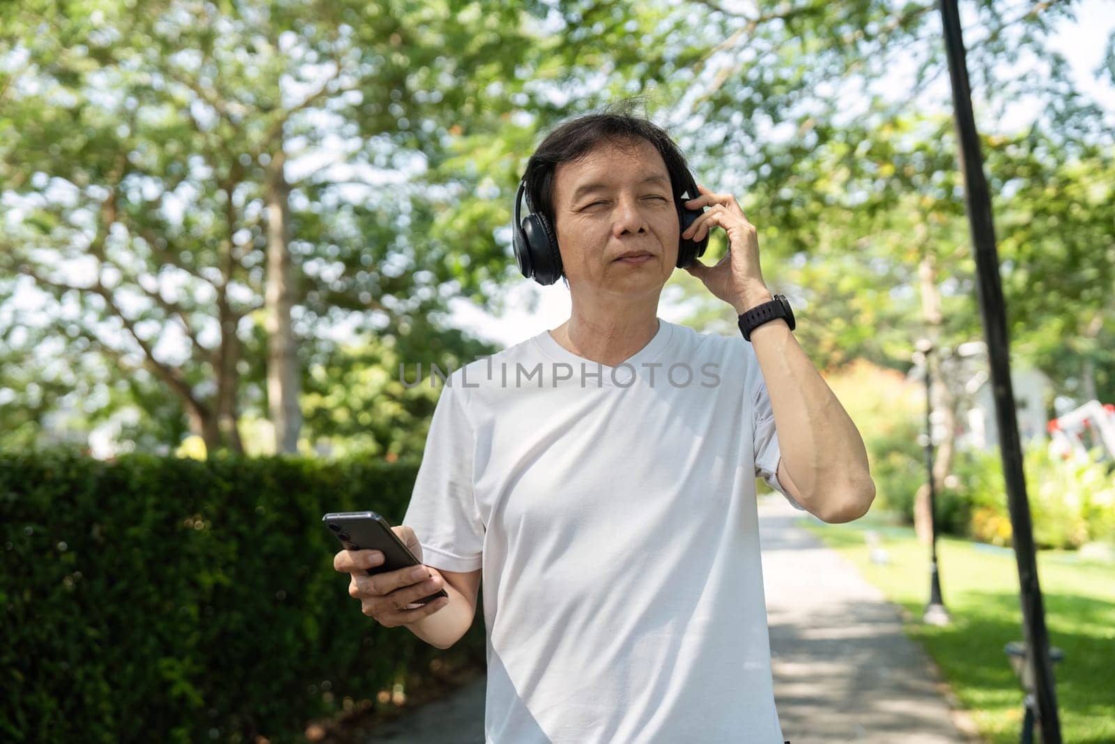 A senior man listens to music with headphones while walking in a park, promoting wellness and outdoor activity.