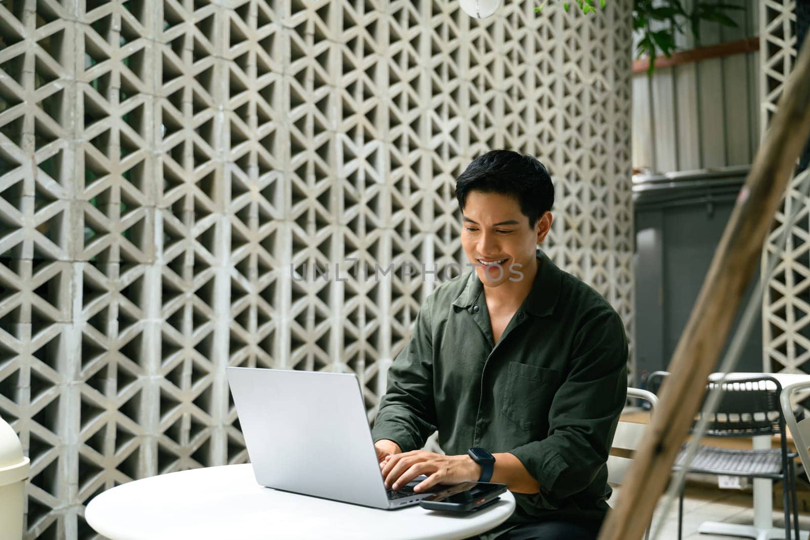 Smiling adult businessman working on his laptop at an outdoor cafe in the city.