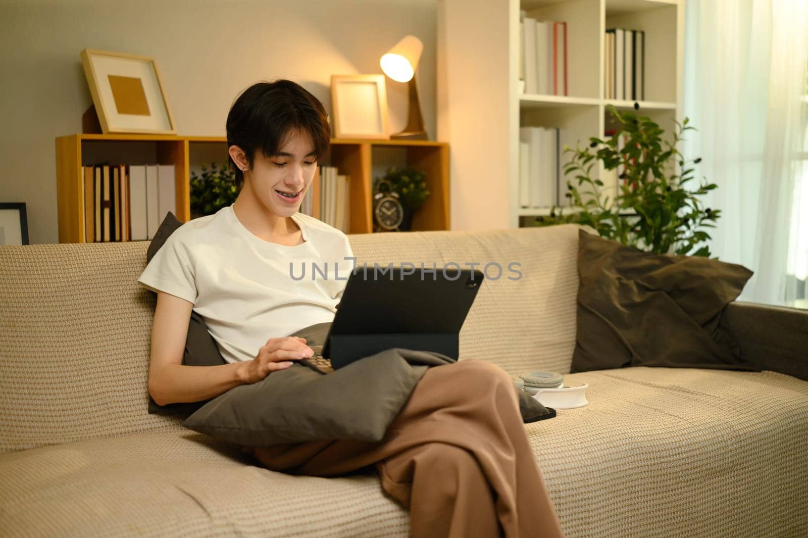 Smiling young man relaxing on sofa while browsing digital tablet at home.