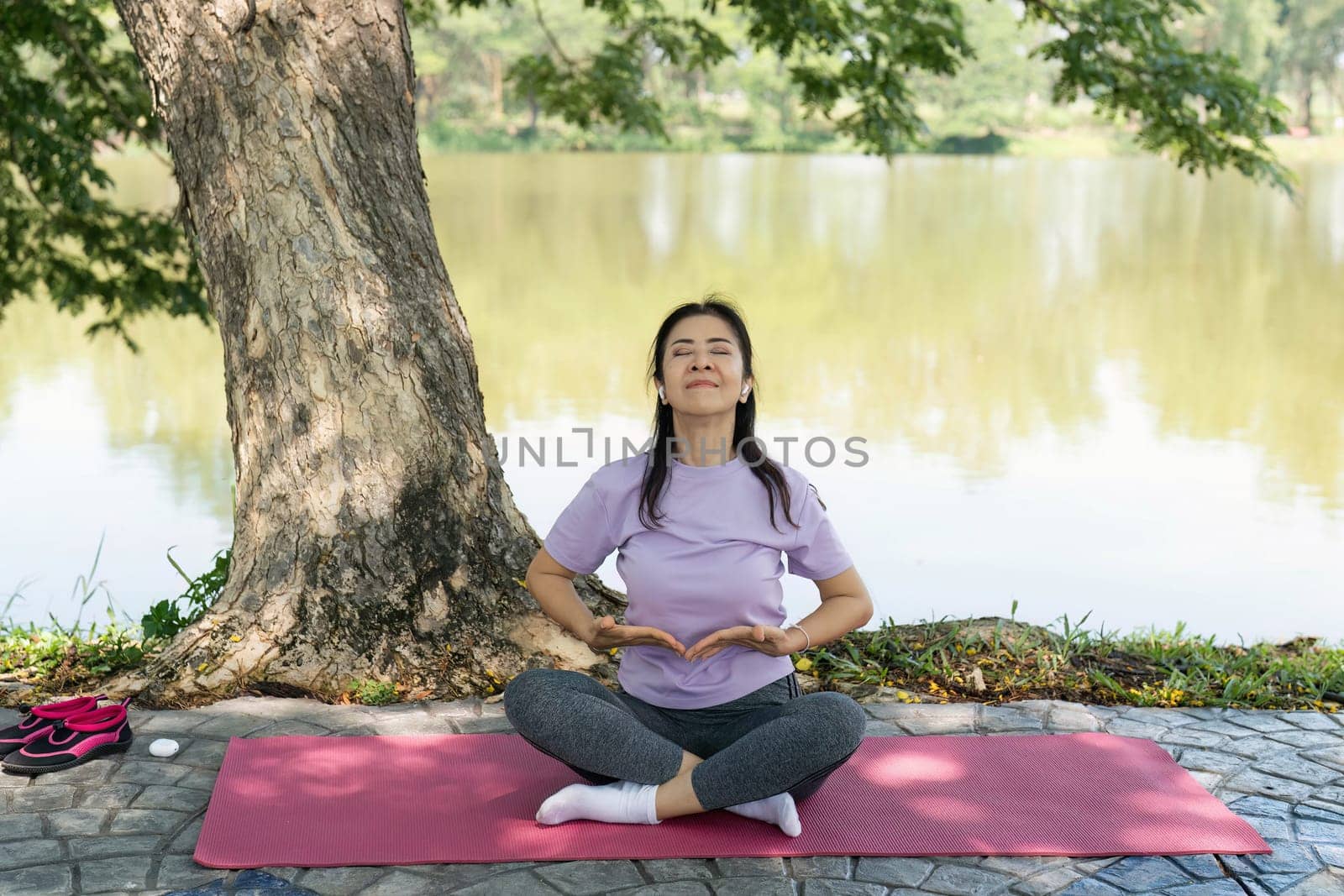 A woman practices yoga and meditation outdoors by a tranquil lake, promoting wellness and mindfulness in nature.