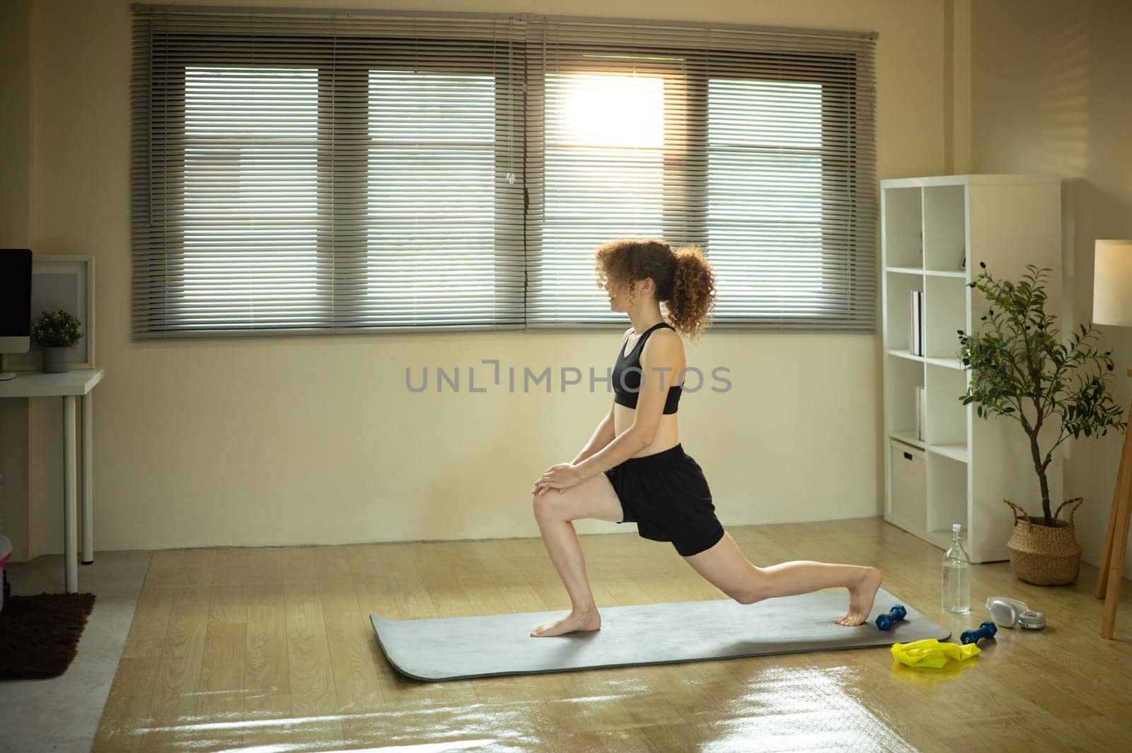 Young Russian woman in activewear doing a lunge stretch on yoga mat in cozy home.